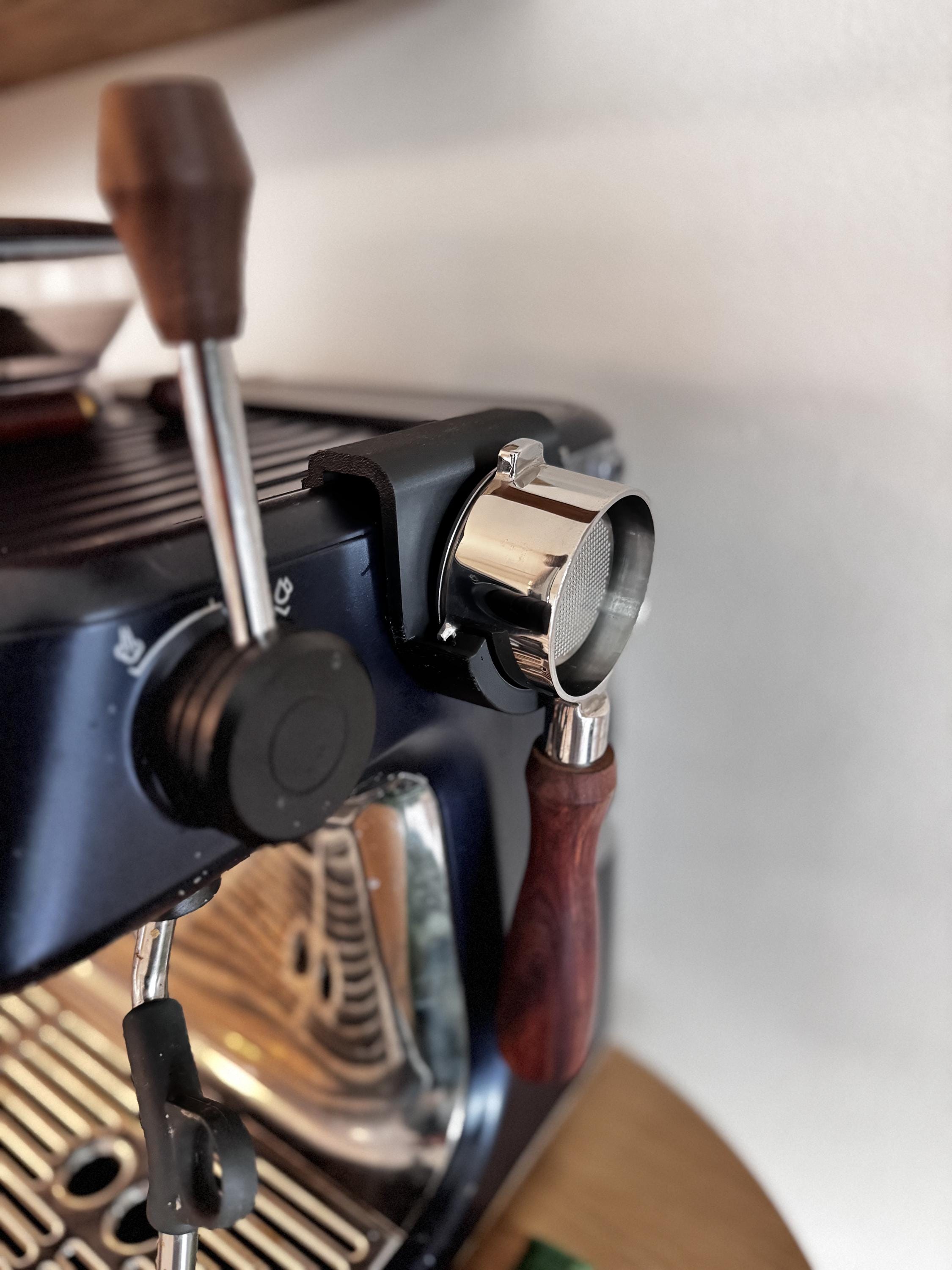 May include: A close-up of a blue espresso machine with a chrome portafilter and a wooden handle. The portafilter is attached to a black bracket.