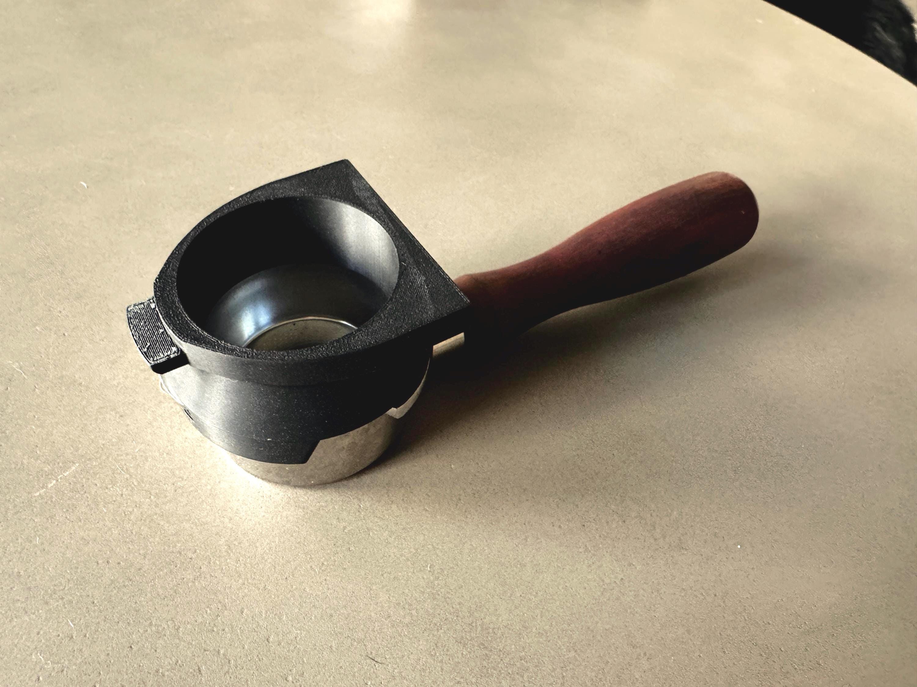 May include: A black and silver espresso portafilter with a wooden handle. The portafilter is designed to hold coffee grounds for brewing espresso.